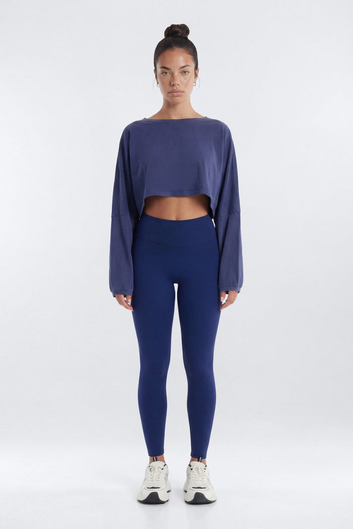 Person wearing a blue long-sleeve crop top and leggings on a white background