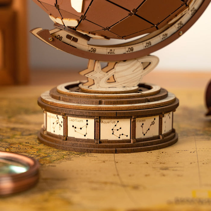 Macro close-up of zodiac constellation engravings laser-cut into the cylindrical base of the wooden globe on a vintage map surface
